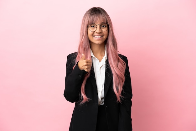 Young business mixed race woman with pink hair isolated on pink background giving a thumbs up gesture