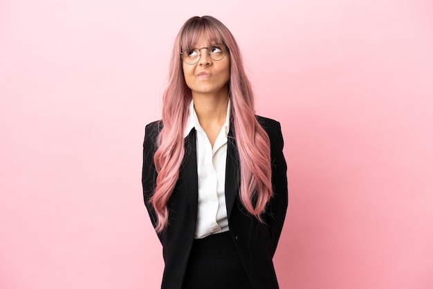 Молодая деловая женщина смешанной расы с розовыми волосами изолирована на розовом фоне и смотрит вверх