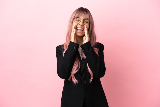 Young business mixed race woman with pink hair isolated on pink background shouting and announcing something