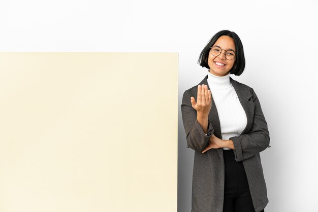 Young business mixed race woman with with a big banner over isolated background inviting to come with hand. Happy that you came