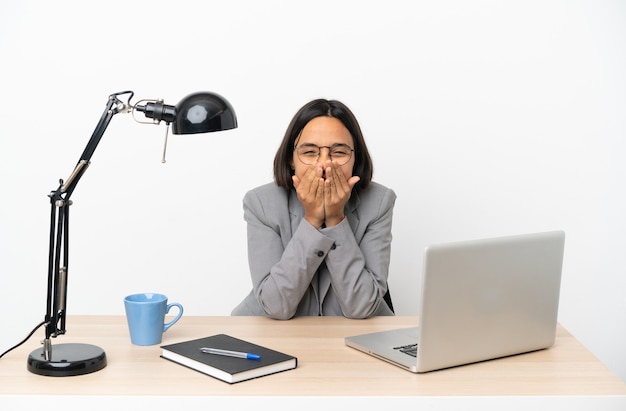 Young business mixed race woman working at office happy and smiling covering mouth with hands