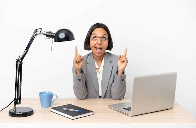 Young business mixed race woman working at office surprised and pointing up