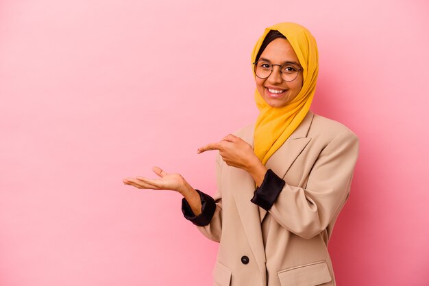 Young business muslim woman isolated on pink background excited holding a copy space on palm.