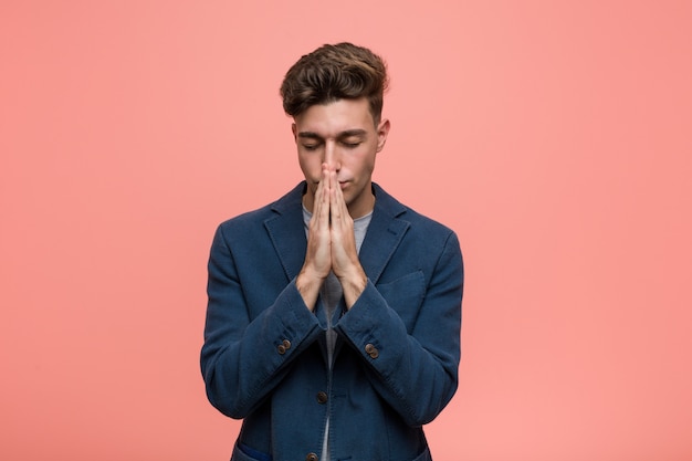 Young business natural man holding hands in pray near mouth, feels confident.