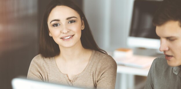 Young business people are talking to each other, while sitting at the desk in sunny office. Businesswoman is explaining something to her colleague.