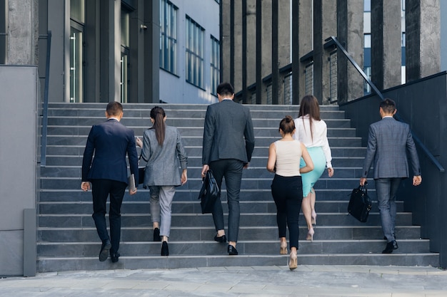 Photo young business people colleagues returning from their break. men and women in formal suits going up stairs into office building. partnership, communication business people concept.