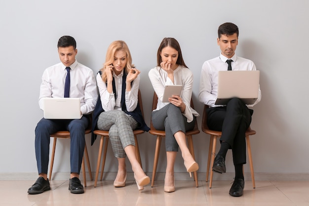 Young business people waiting in line near light wall