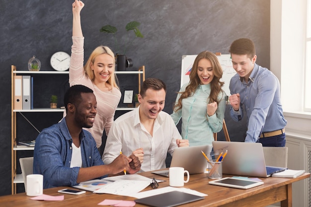 Young business team enjoying success, looking at computer screen, celebrating successful project, dealing contract, winning tender, copy space