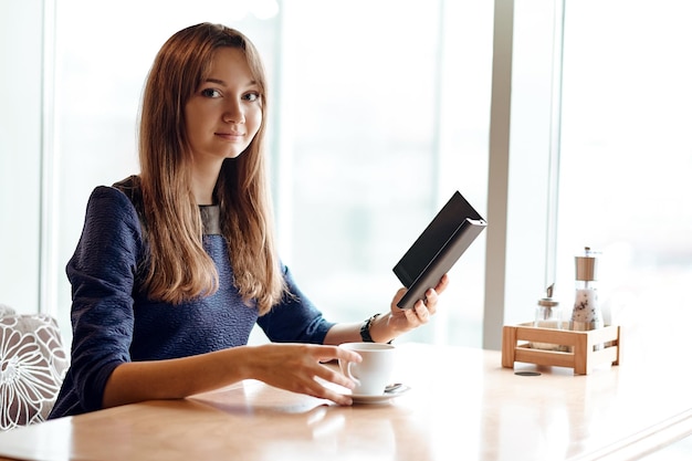 Молодая деловая женщина в кафе читает электронную книгу и пьет кофе