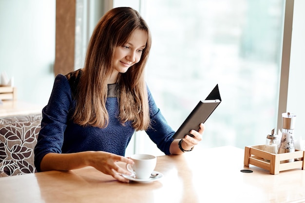 Молодая бизнес-леди в кафе читает электронную книгу и пьет кофе