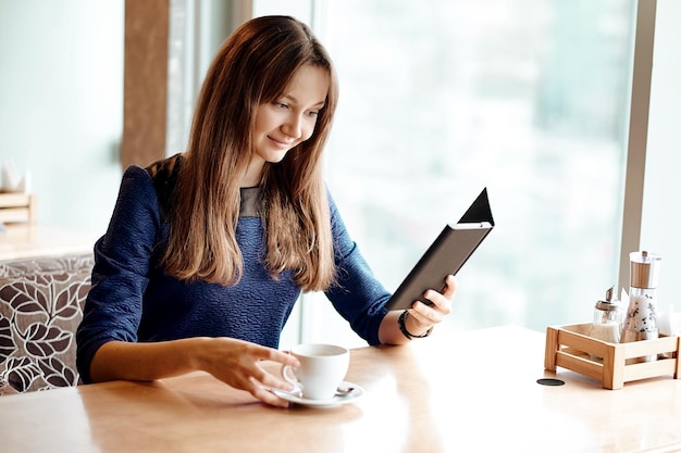 電子書籍を読んで、コーヒーを飲みながらカフェで若いビジネス女性