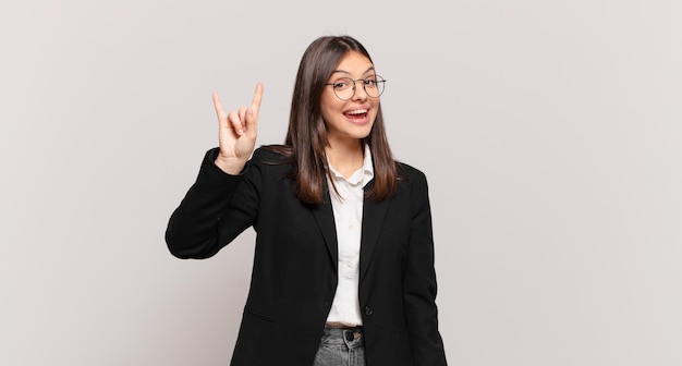 Young business woman feeling happy, fun, confident, positive and rebellious, making rock or heavy metal sign with hand