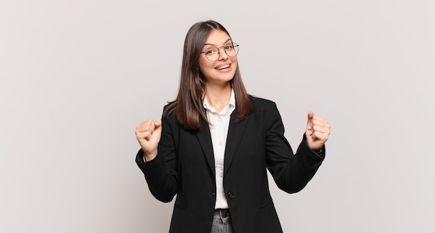 Young business woman feeling happy, positive and successful, celebrating victory, achievements or good luck