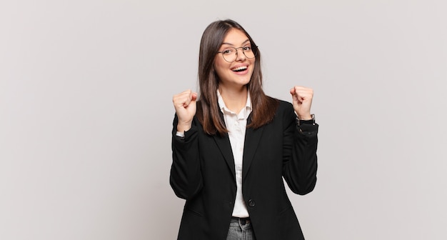 Young business woman feeling shocked, excited and happy, laughing and celebrating success, saying wow!