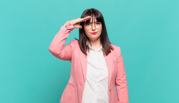 Young business woman greeting the camera with a military salute in an act of honor and patriotism, showing respect