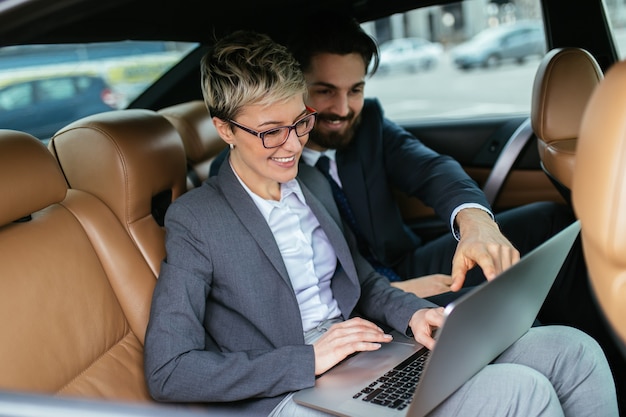 Young business woman and her assistant sitting in limousine talking and working.