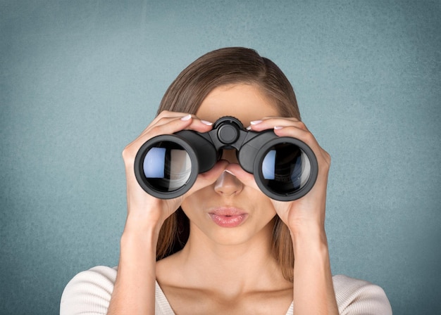 Young business woman holding binoculars on blurred office background