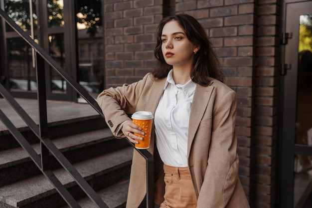 Giovane donna d'affari che tiene il caffè del moderno edificio per uffici sullo sfondo