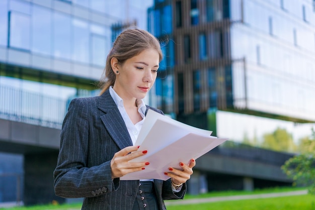 Young business woman holding papers in business clothes on city street against