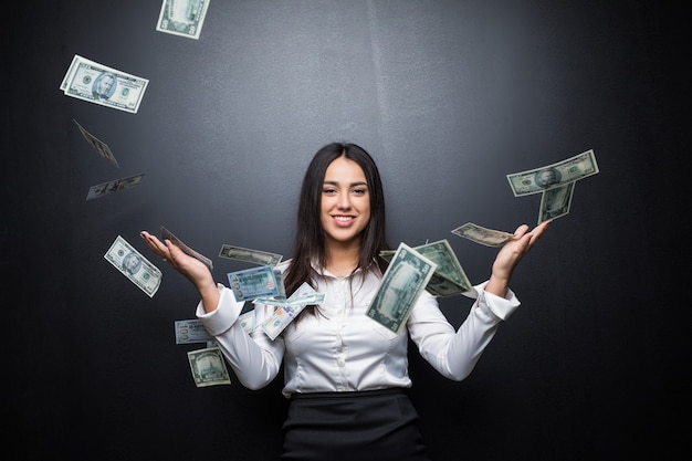 Young Business woman is standing in the rain of the dollar bills on black wall