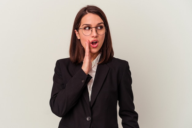 Young business woman isolated on white background is saying a secret hot braking news and looking aside