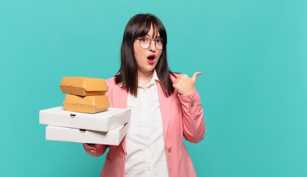 Young business woman looking astonished in disbelief, pointing at object on the side and saying wow, unbelievable