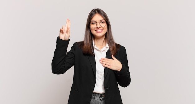 Young business woman looking happy, confident and trustworthy, smiling and showing victory sign, with a positive attitude