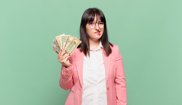 Young business woman looking puzzled and confused, biting lip with a nervous gesture, not knowing the answer to the problem