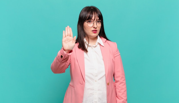 Young business woman looking serious, stern, displeased and angry showing open palm making stop gesture