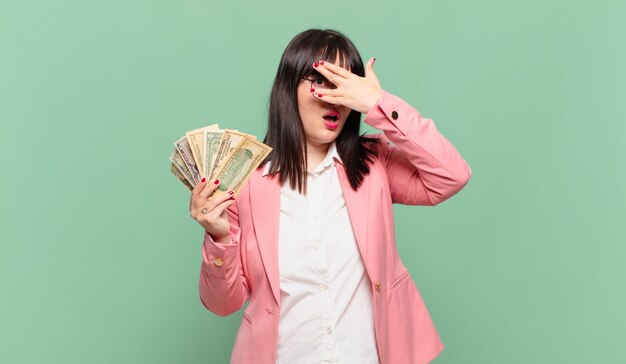 Young business woman looking shocked, scared or terrified, covering face with hand and peeking between fingers