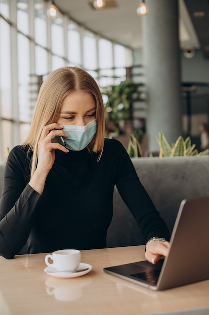 Giovane donna di affari nella maschera che lavora al computer portatile in un caffè