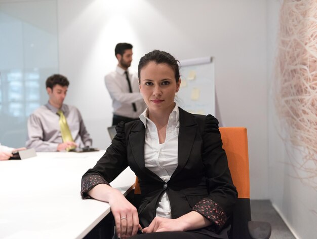 молодая деловая женщина на встрече использует портативный компьютер, размыла группу людей на заднем плане в современном ярком интерьере офиса стартапа, делая заметки на белой доске и проводя мозговой штурм о планах