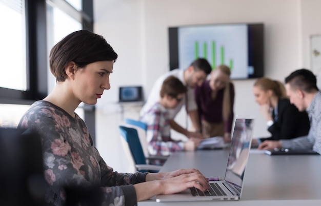 молодая деловая женщина в современном интерьере офиса стартапа, работающая на ноутбуке, размытая команда на встрече, группа людей на заднем плане