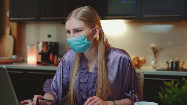 Photo young business woman in protective mask working at home on quarantine.