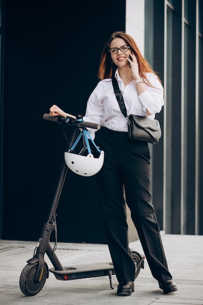 Young business woman riding scooter and using phone