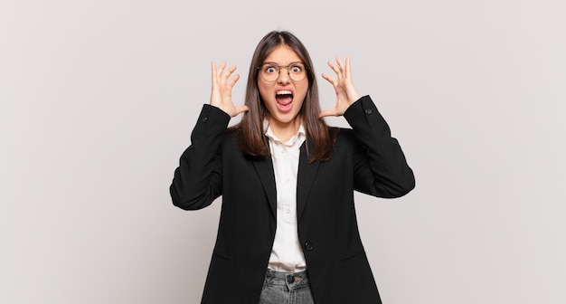 Young business woman screaming with hands up in the air, feeling furious, frustrated, stressed and upset