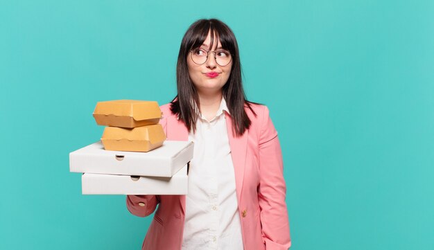 Young business woman shrugging, feeling confused and uncertain, doubting with arms crossed and puzzled look