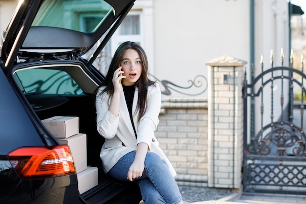 Young business woman sitting in the car coming home by car The girl is sitting in the car and talking on mobile phone Concept of buying goods online and delivering them home