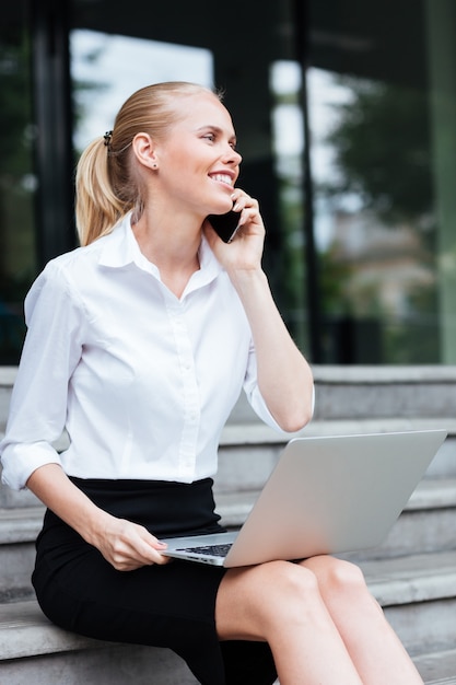 Young business woman sitting on stairs and talking on cell phone outdoors