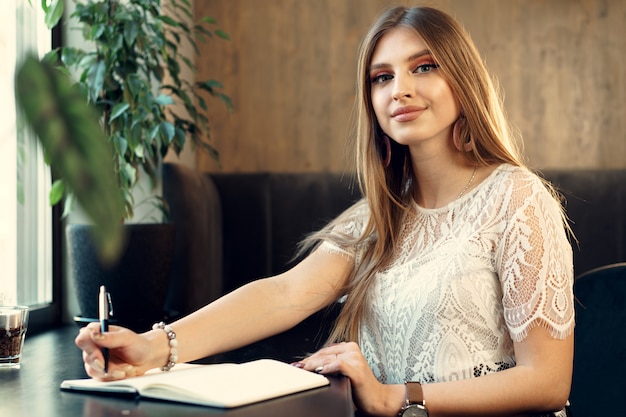 Young business woman sitting at the table in a coffee shop and making notes