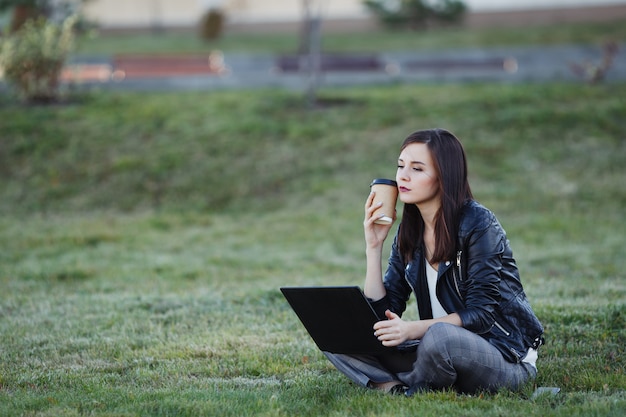 Young business woman sitting and working in park with laptop