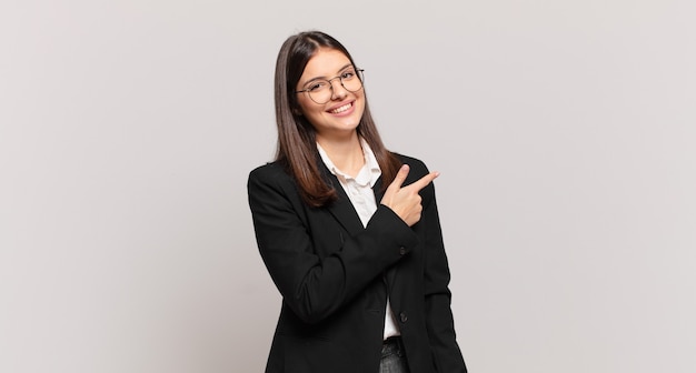 young business woman smiling cheerfully, feeling happy and pointing to the side and upwards, showing object in copy space