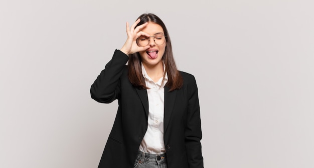 Young business woman smiling happily with funny face, joking and looking through peephole, spying on secrets