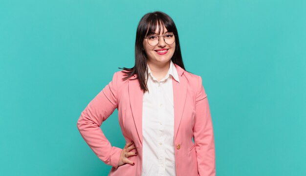 Young business woman smiling happily with a hand on hip and confident, positive, proud and friendly attitude