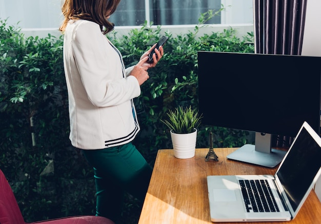 Young business woman stand using smart phone calling to customer on her working with laptop computer