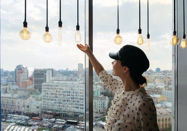 Young business woman standing by the window enjoying the city skyline with stunning panoramic view and bulbs