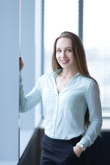 Молодая деловая женщина, стоящая у окна в коридоре офиса.