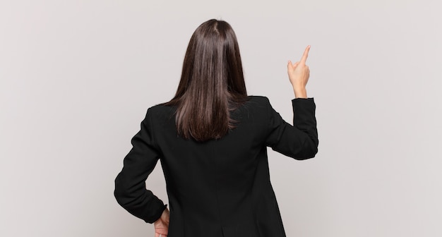 Young business woman standing and pointing to object on copy space, rear view