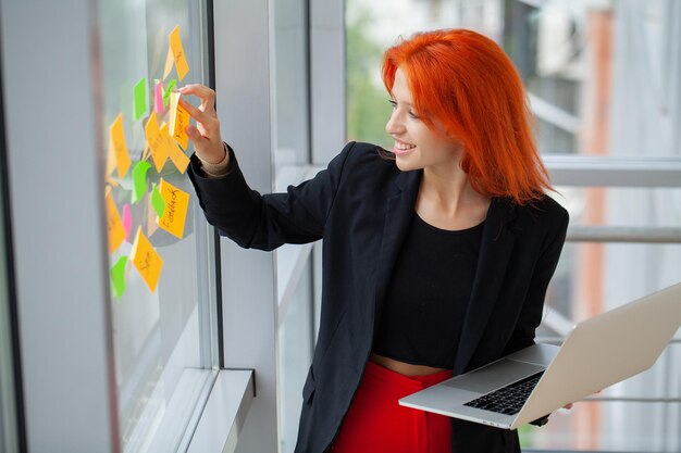 Young business woman standing with a laptop in his office near the background of a window