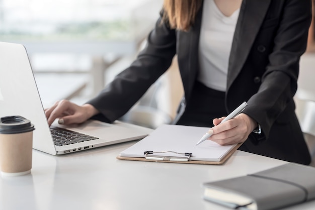 Giovane donna d'affari prendere appunti e utilizzare un computer portatile in ufficio.